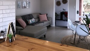 Una sala de estar moderna con un sofá gris, una mesa de centro de madera y un comedor con una mesa pequeña y sillas.