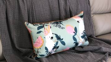 A sofa with a grey blanket and a cushion with a bird and floral pattern.