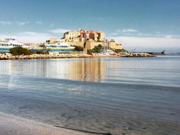 Une ville côtière qui se distingue par un imposant bâtiment ressemblant à un château, une mer calme et une côte rocheuse.