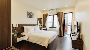 A hotel room with a large bed, a desk with a lamp, a plant, and a view of the outside through a window. - Paragon House & Residence (Hanoi)