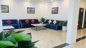 A modern lobby with a blue sofa set, a marble coffee table, and large potted plants. - Paragon House & Residence (Hanoi)