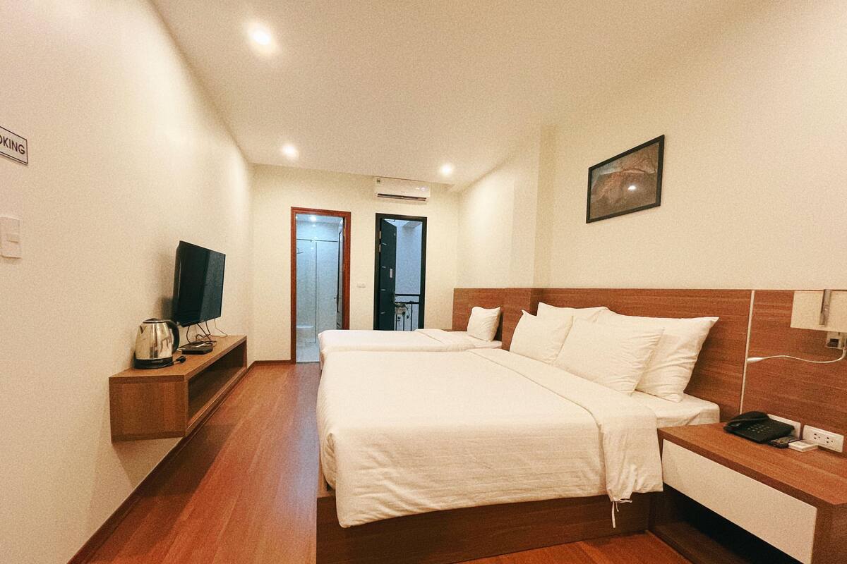 A hotel room with two beds, a TV, a bedside table, and a small cabinet.