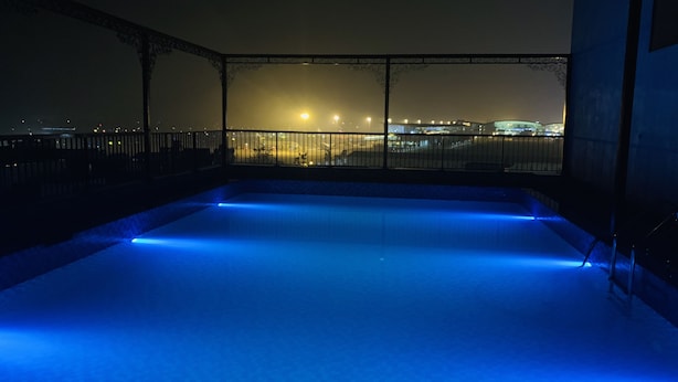 A rooftop pool with blue lighting, surrounded by a metal railing and overlooking a cityscape at night. - Paragon House & Residence (Hanoi)