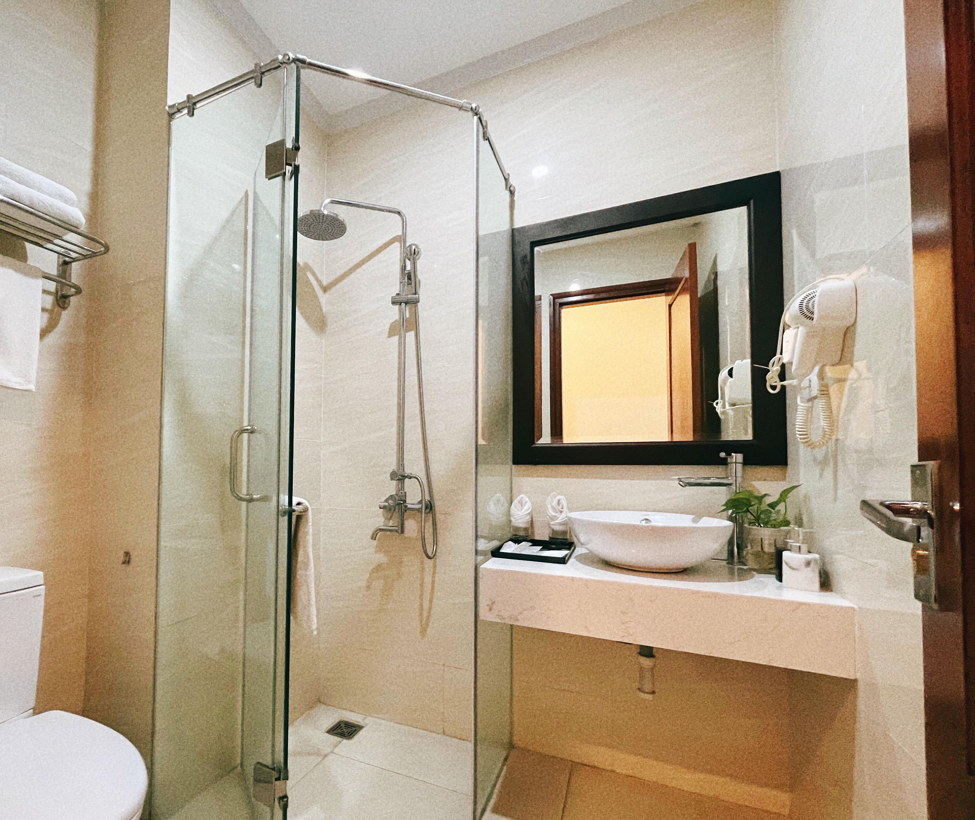 A bathroom with a glass-enclosed shower, a toilet, and a sink with a mirror above it.