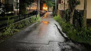 A narrow street with buildings on either side, a wet surface, and overhead power lines.
