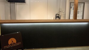 A modern reception area with a wooden counter, overhead lighting, and a sign for 'Arura Sapporo Hostel and Guesthouse'. - Arura Sapporo - Hostel (Sapporo)