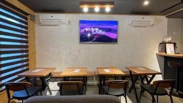 A conference room with tables and chairs, a mounted TV screen, and a ceiling light fixture.