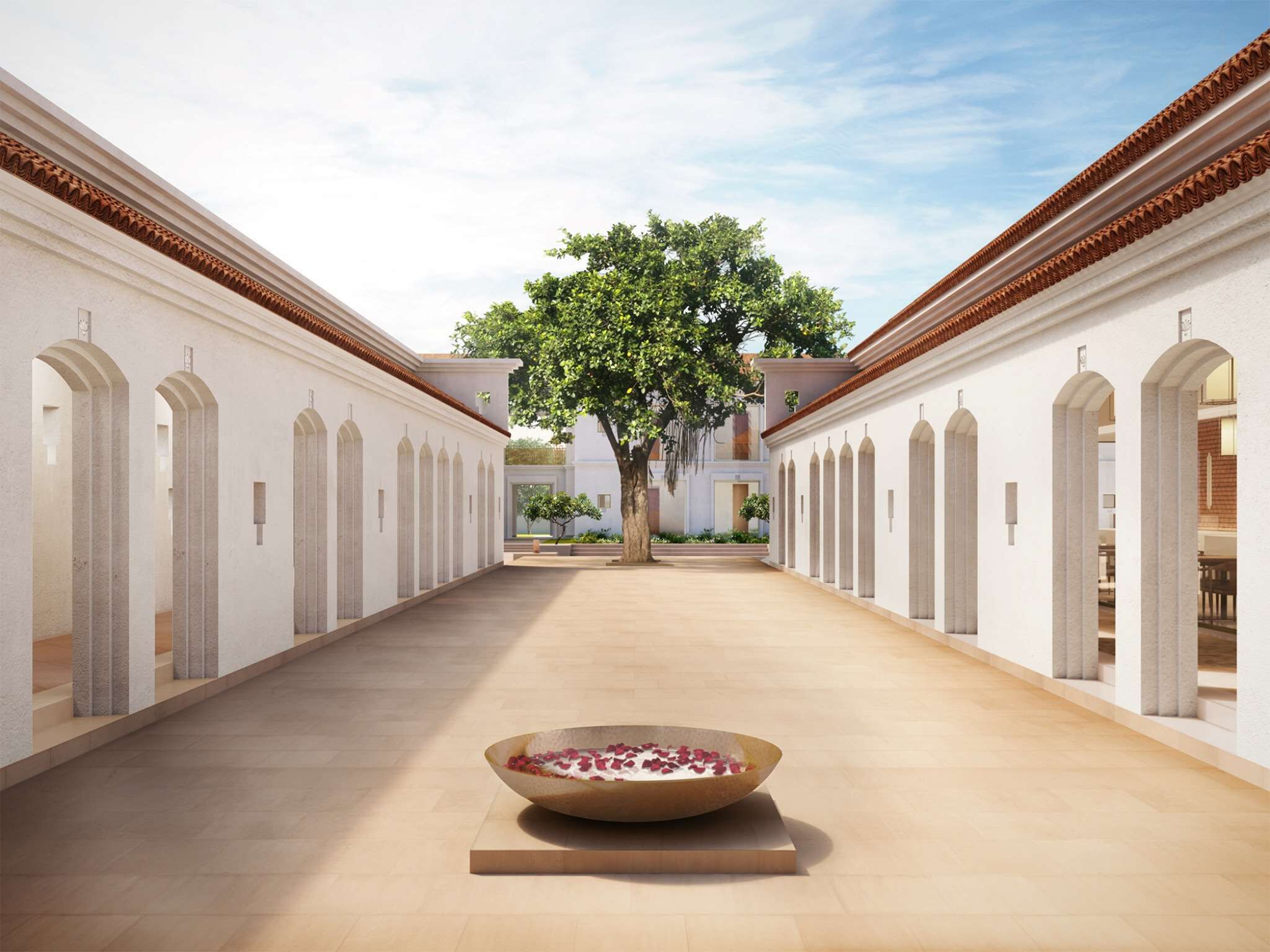 A corridor with a central decorative bowl, flanked by white walls with arches and a tree in the background.