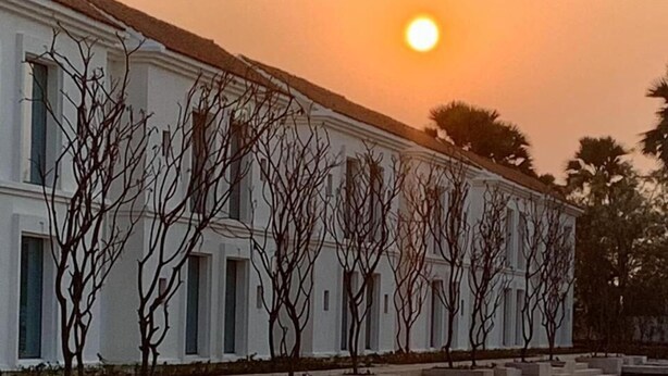 Un edificio con un estanque reflectante, árboles despojados de hojas y una puesta de sol.