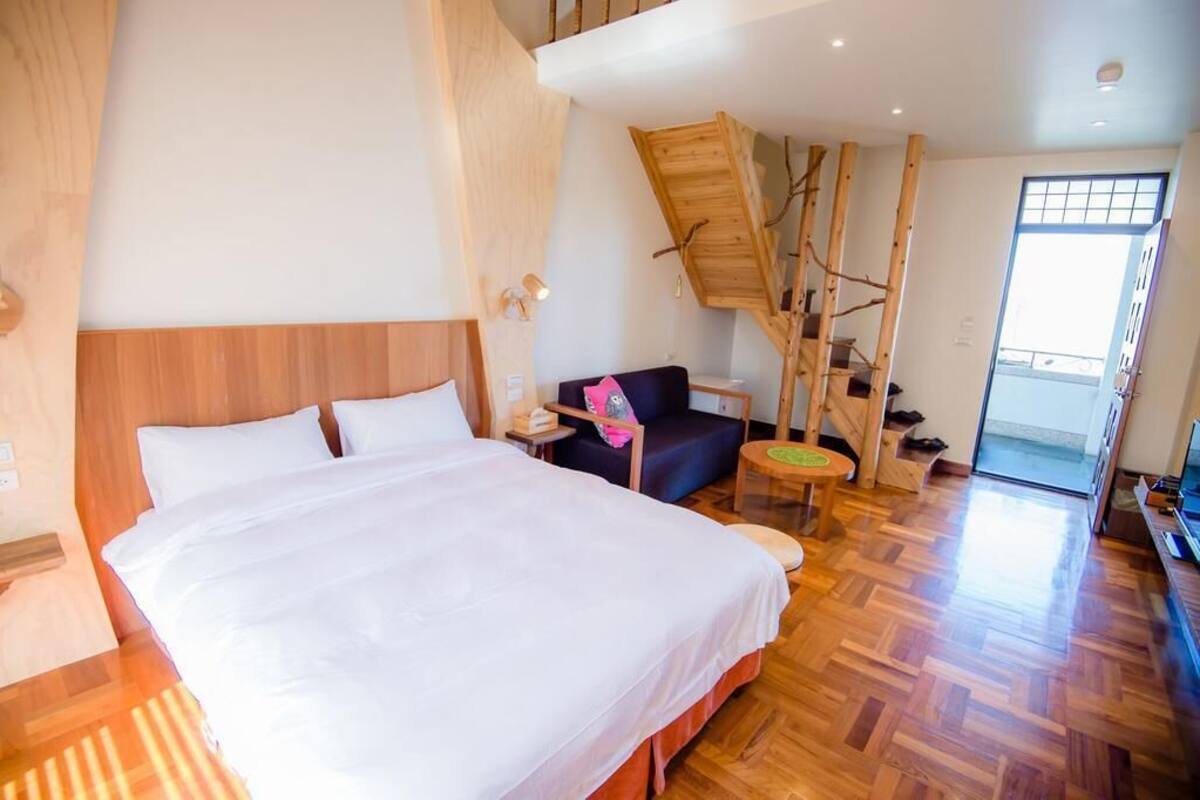 A hotel room with a large bed, a wooden staircase, a small round table, and a sofa.