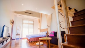 A modern hotel room with a wooden staircase, a bed with a blue headboard, a round table, and a sofa with a pink pillow.