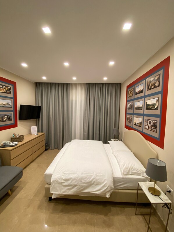 A hotel room with a bed, a desk, a chair, a TV, and a wall with pictures.