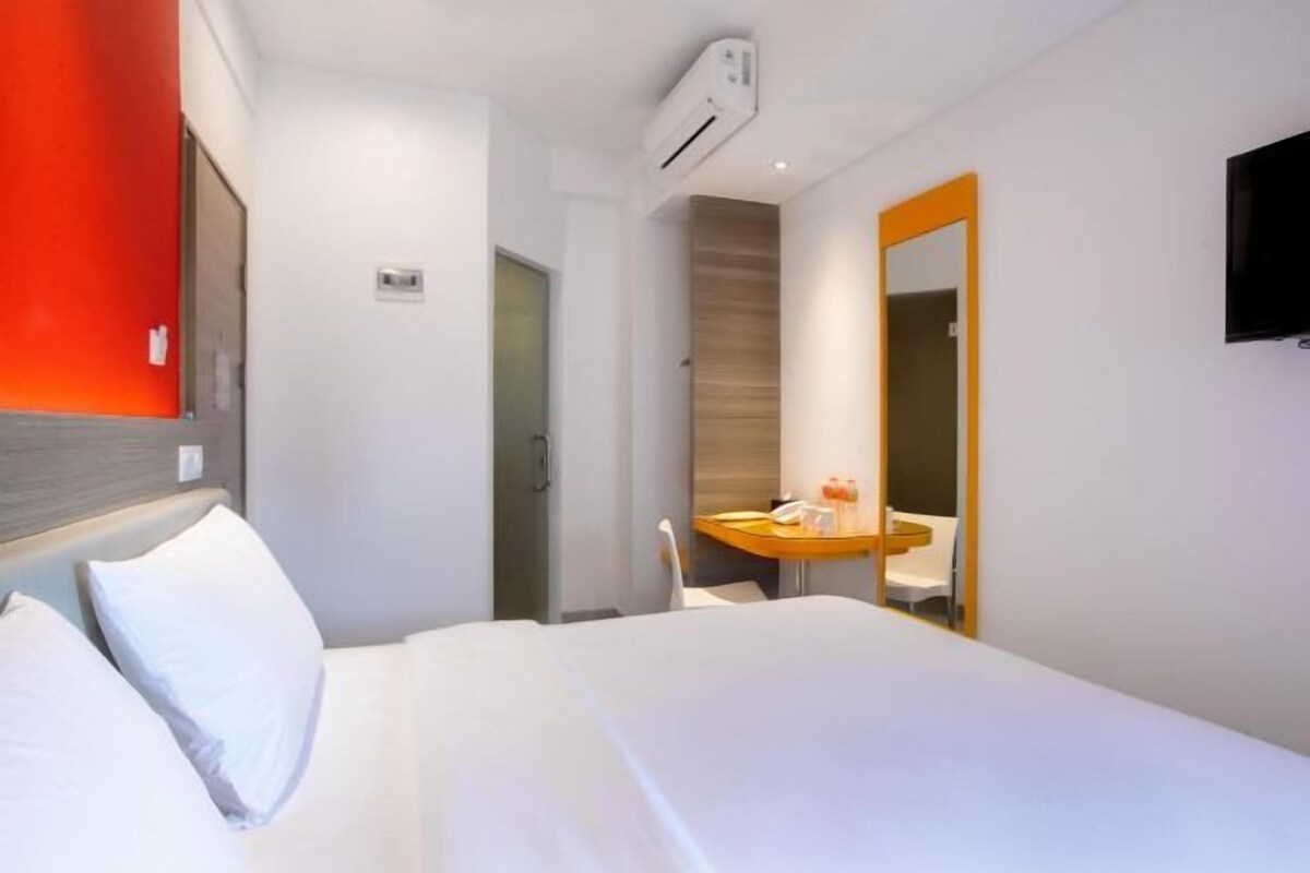 A hotel room with a bed, a desk, a chair, a mirror, and a TV.