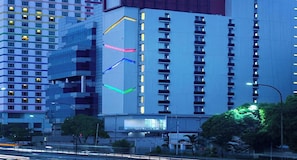 Un edificio a più piani con un design architettonico moderno, caratterizzato da una struttura verticale importante con linee illuminate e un grande cartellone pubblicitario alla base.