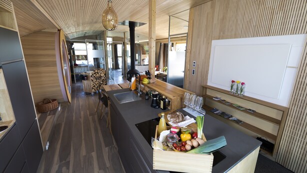 Une cuisine moderne agrémentée d’éléments en bois, un îlot central où sont disposés des produits frais, et une vue sur l’espace de vie.
