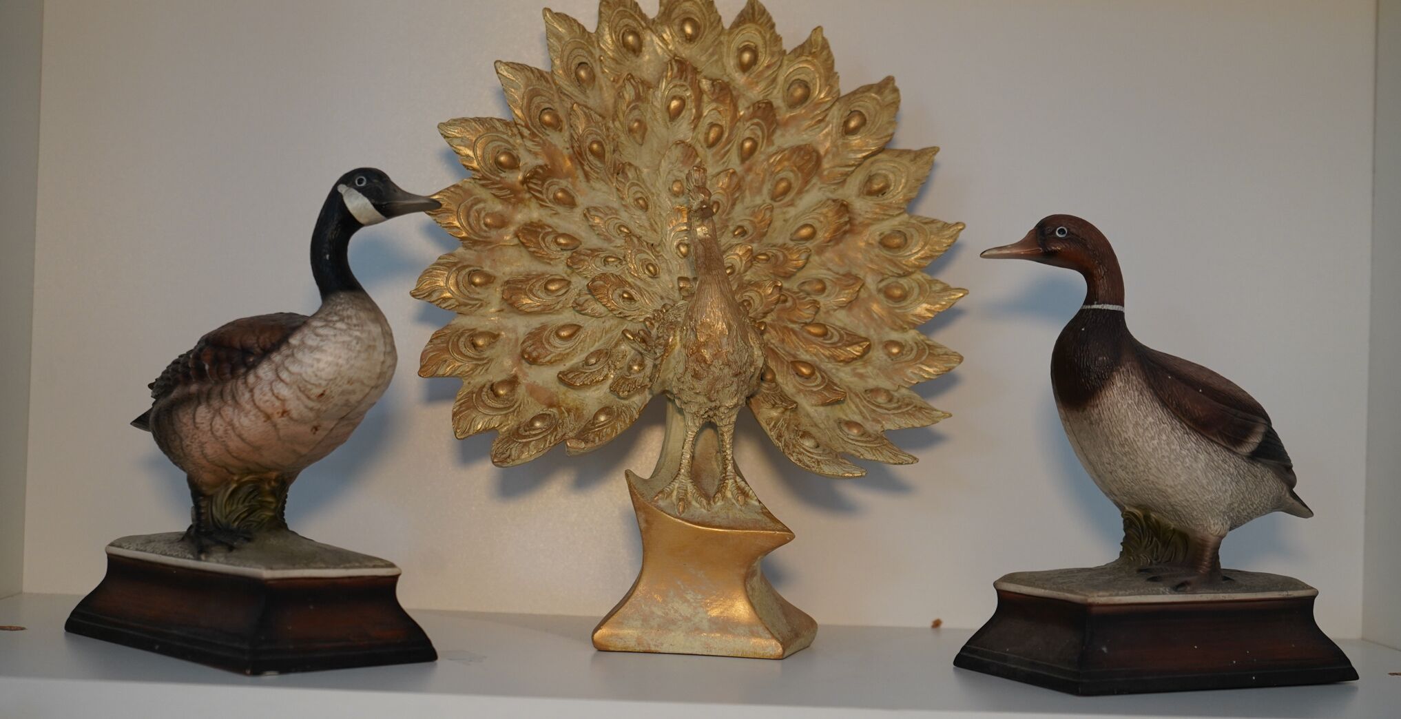 Tres esculturas de pájaros sobre una repisa, cada una sobre un pedestal oscuro, con un árbol dorado decorativo en el centro.