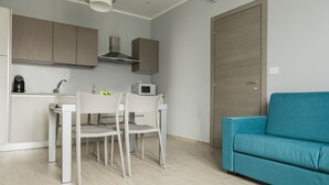 Une cuisine moderne avec des meubles blancs, un four à micro-ondes et une machine à café. On y trouve également un canapé de couleur turquoise et une table à manger avec des chaises.
