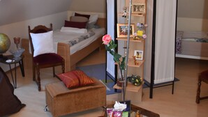Een gezellig loft-slaapkamer met een schuine kap, een grote kroonluchter, een houten boekenkast, een klein bureau en een comfortabele zithoek.