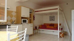 A compact room with a bunk bed, kitchenette, and a dining area.