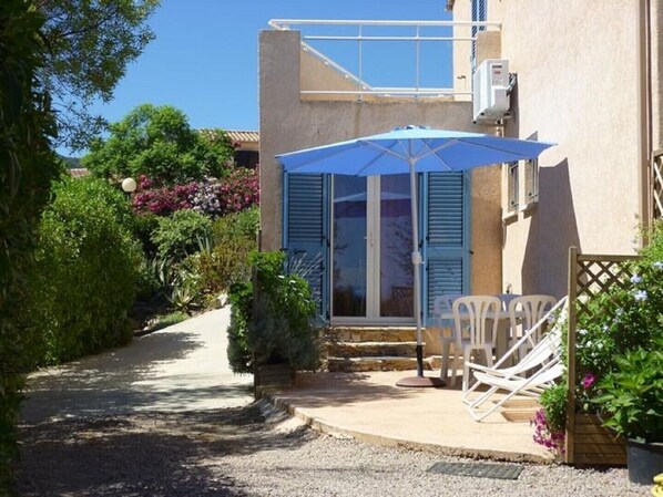A pathway leading to a building with a blue awning and a white chair outside.