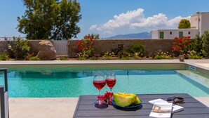 Escena junto a la piscina con una mesa que tiene dos copas de vino tinto, un melón y algunas lecturas.