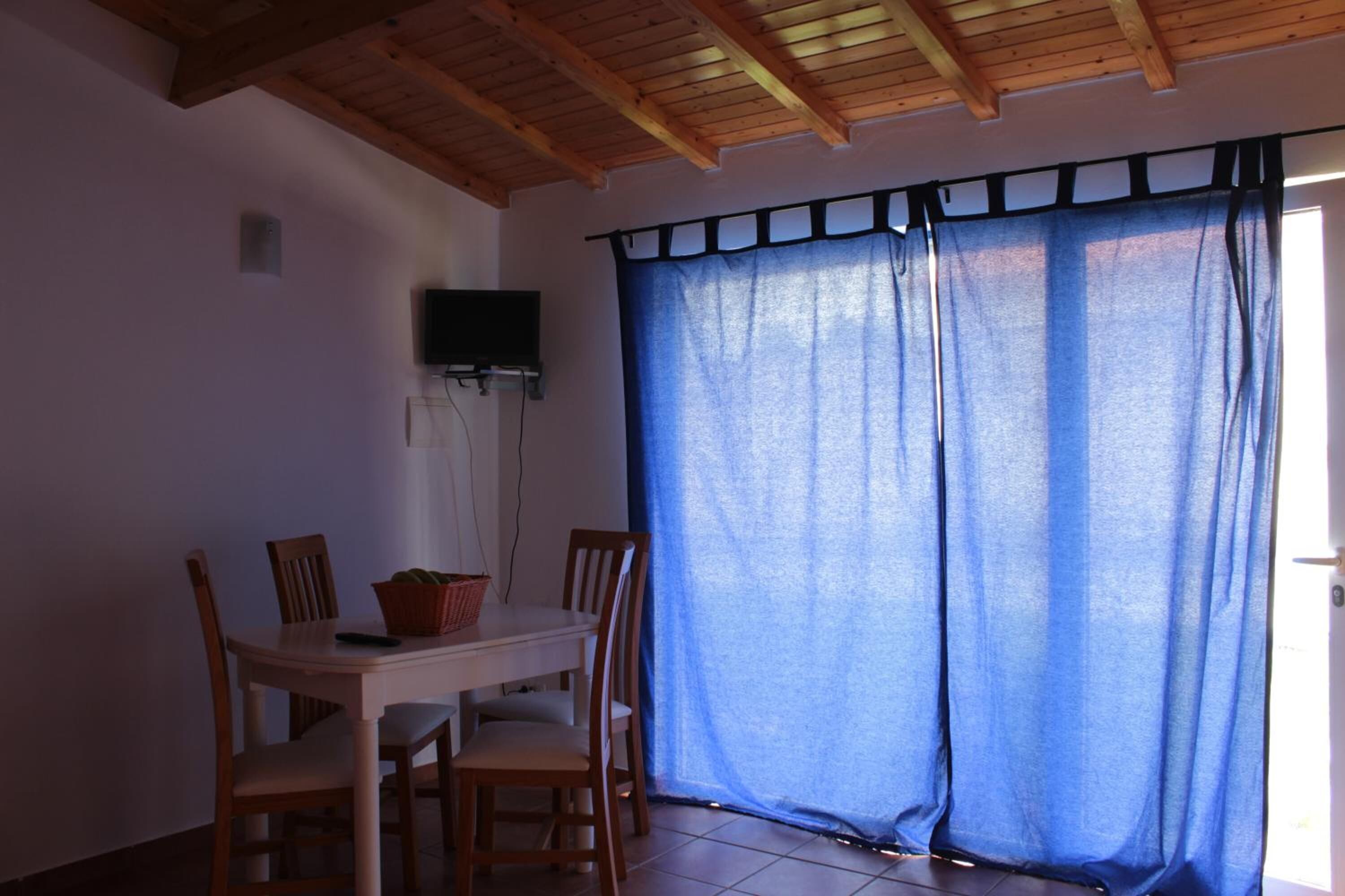 Un comedor con una mesa y sillas de madera, una cesta sobre la mesa, y una cortina azul que cubre una ventana.