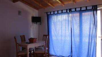 Un comedor con una mesa y sillas de madera, una cesta sobre la mesa, y una cortina azul que cubre una ventana.
