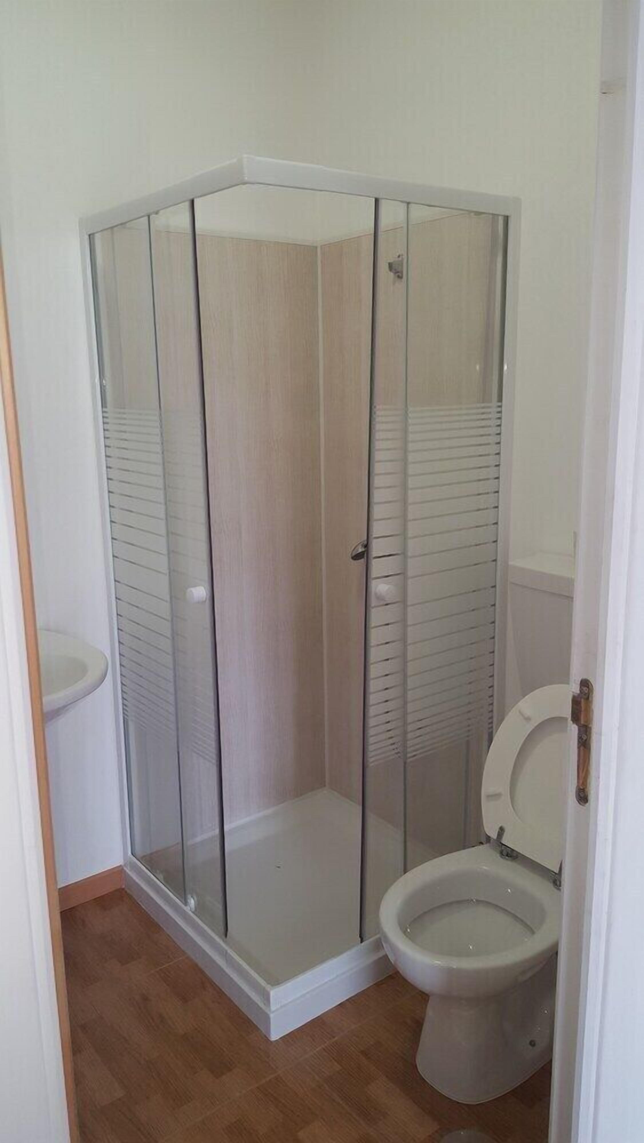 A corner shower with glass doors and a toilet.