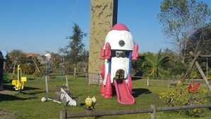 A playground with a slide and climbing structures, surrounded by grass and trees. - Quinta do Valão (Alcobaça)