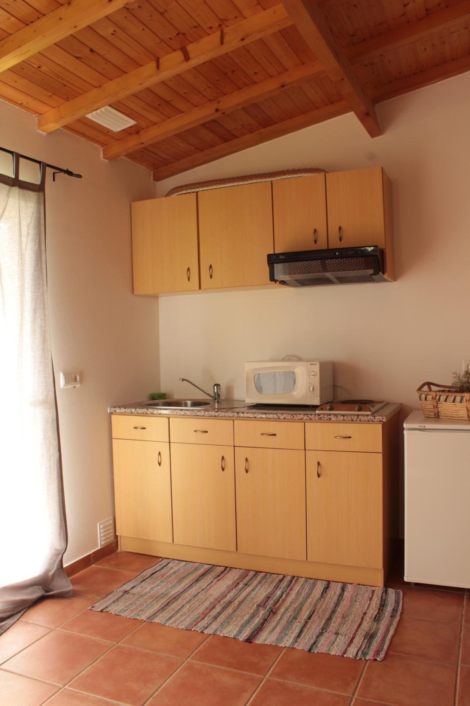 A compact kitchen with wooden cabinets, a microwave, and a small refrigerator.