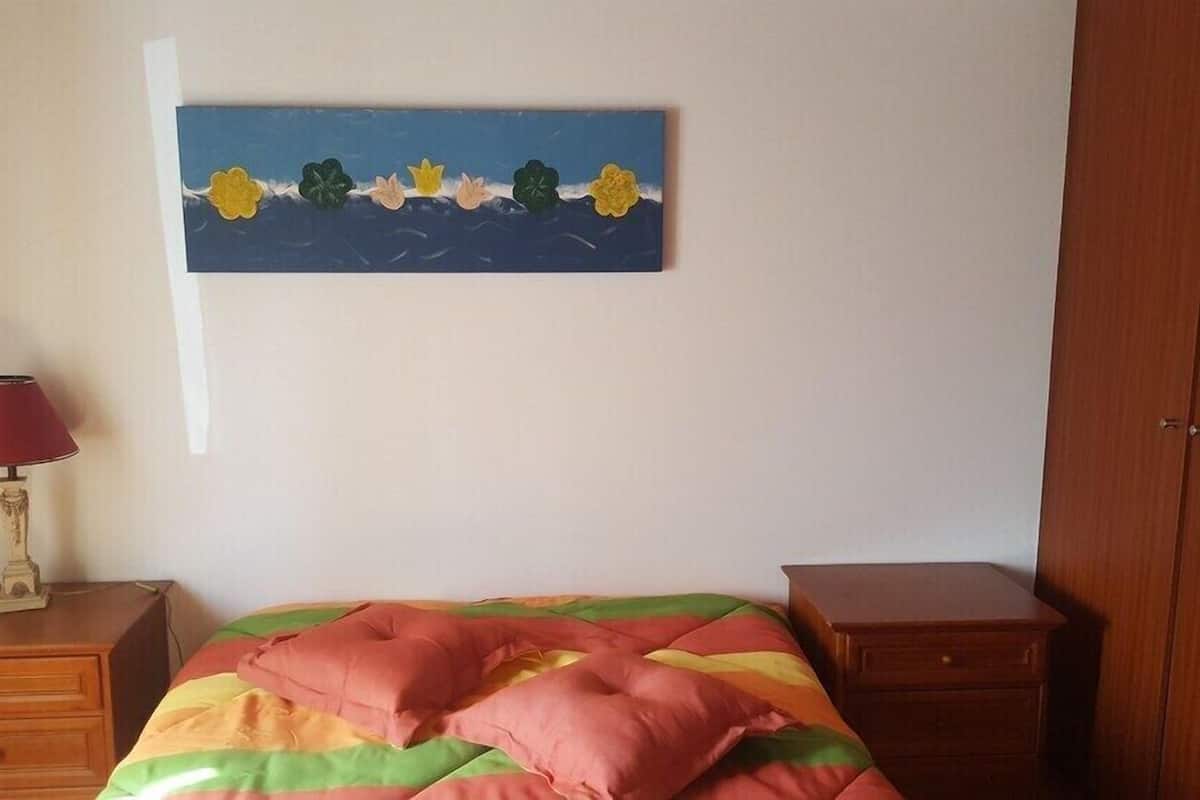 Un dormitorio con una cama, una mesita de noche con una lámpara, un armario de madera y un cuadro en la pared.