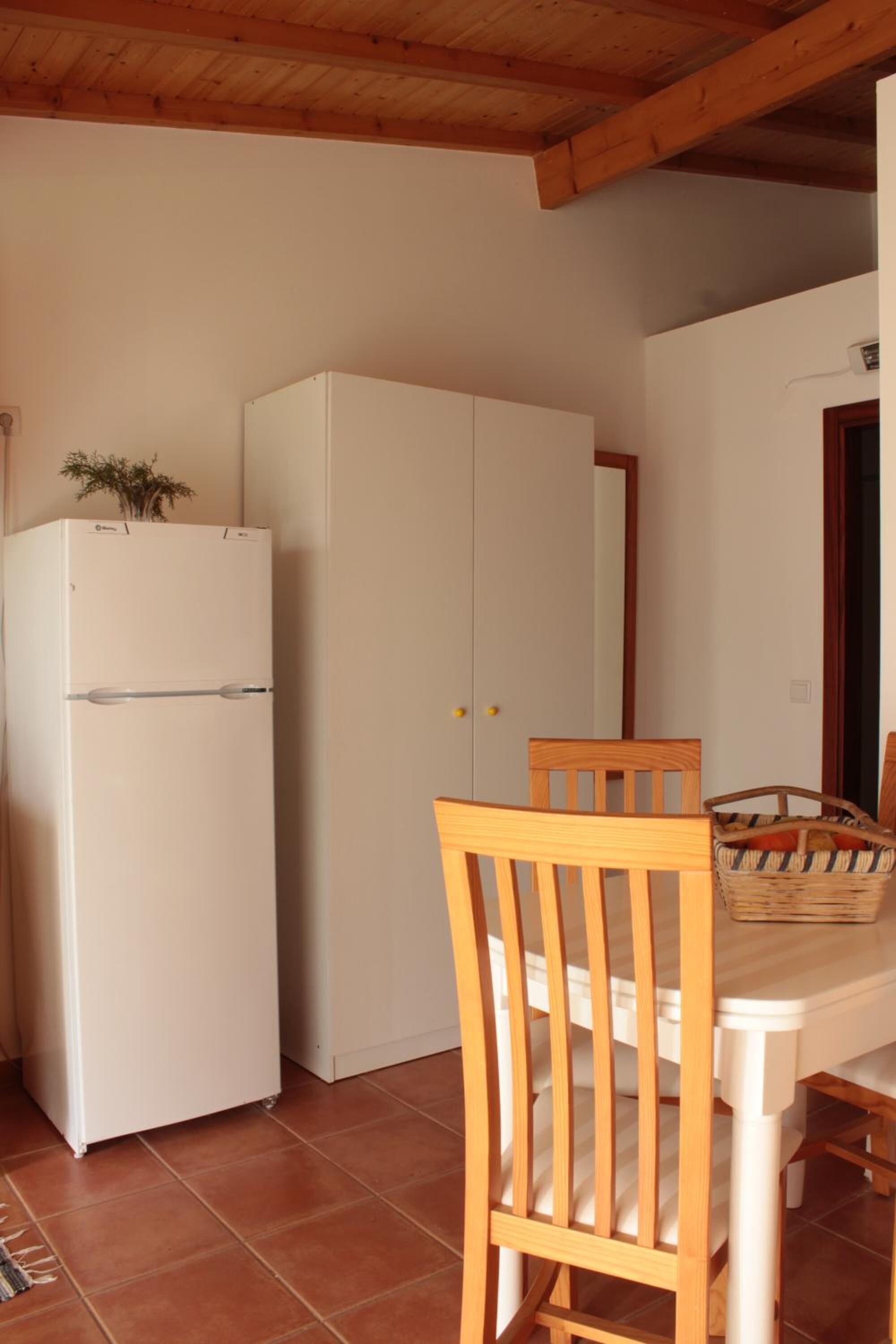 Una cocina con un refrigerador blanco, sillas de madera, una mesa de comedor y piso de baldosas.