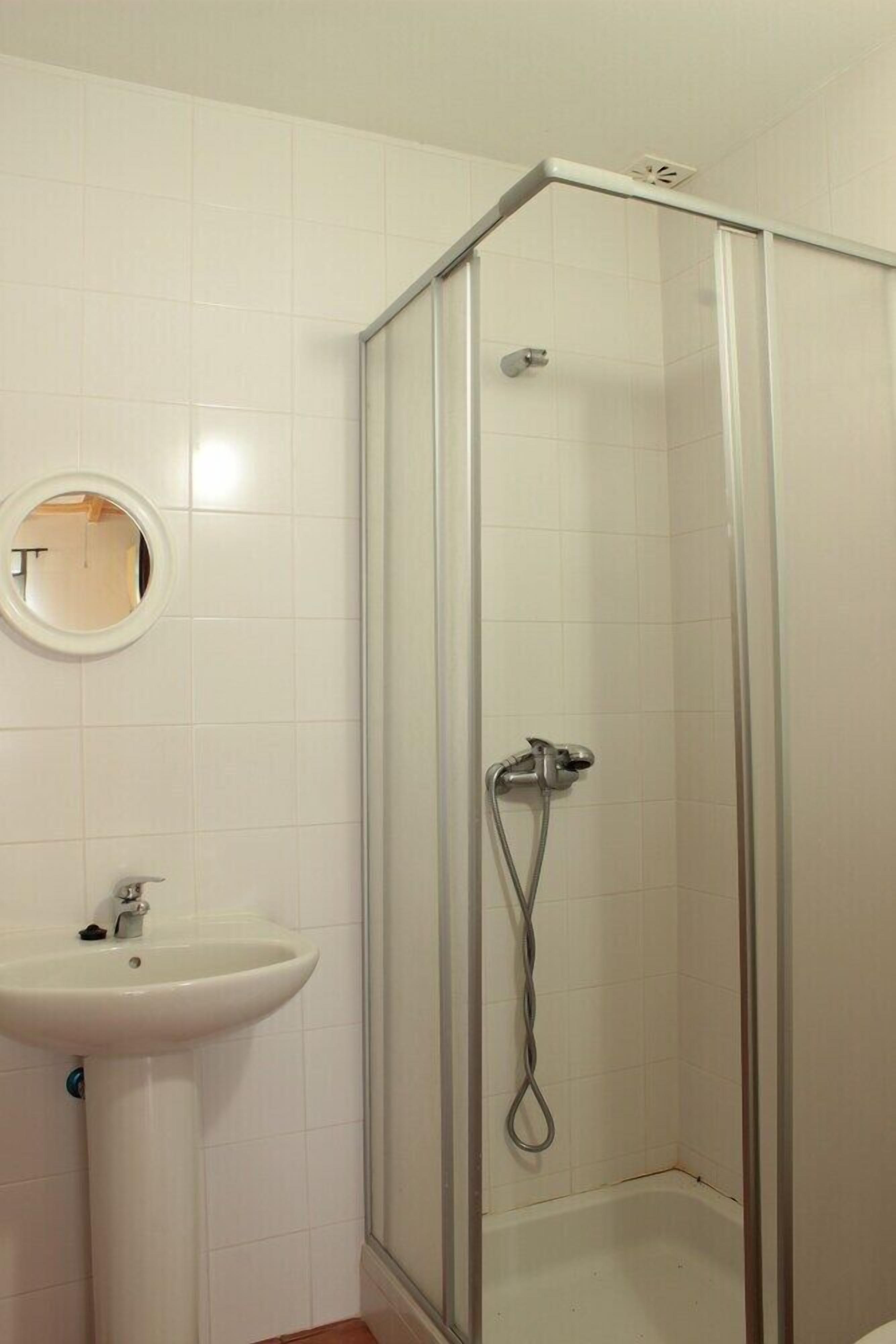 A bathroom with a glass-enclosed shower, a white sink, and a round mirror on the wall.