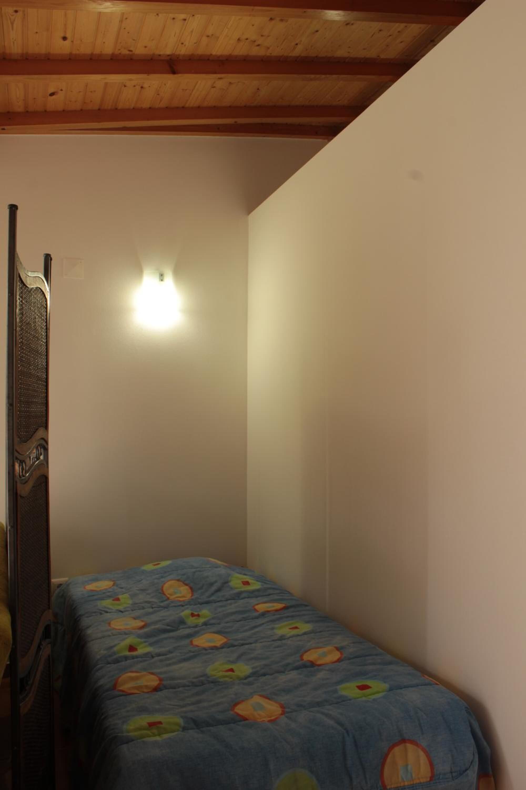 A small bedroom with a single bed, a wooden headboard, a wall-mounted light, and a sloped ceiling.
