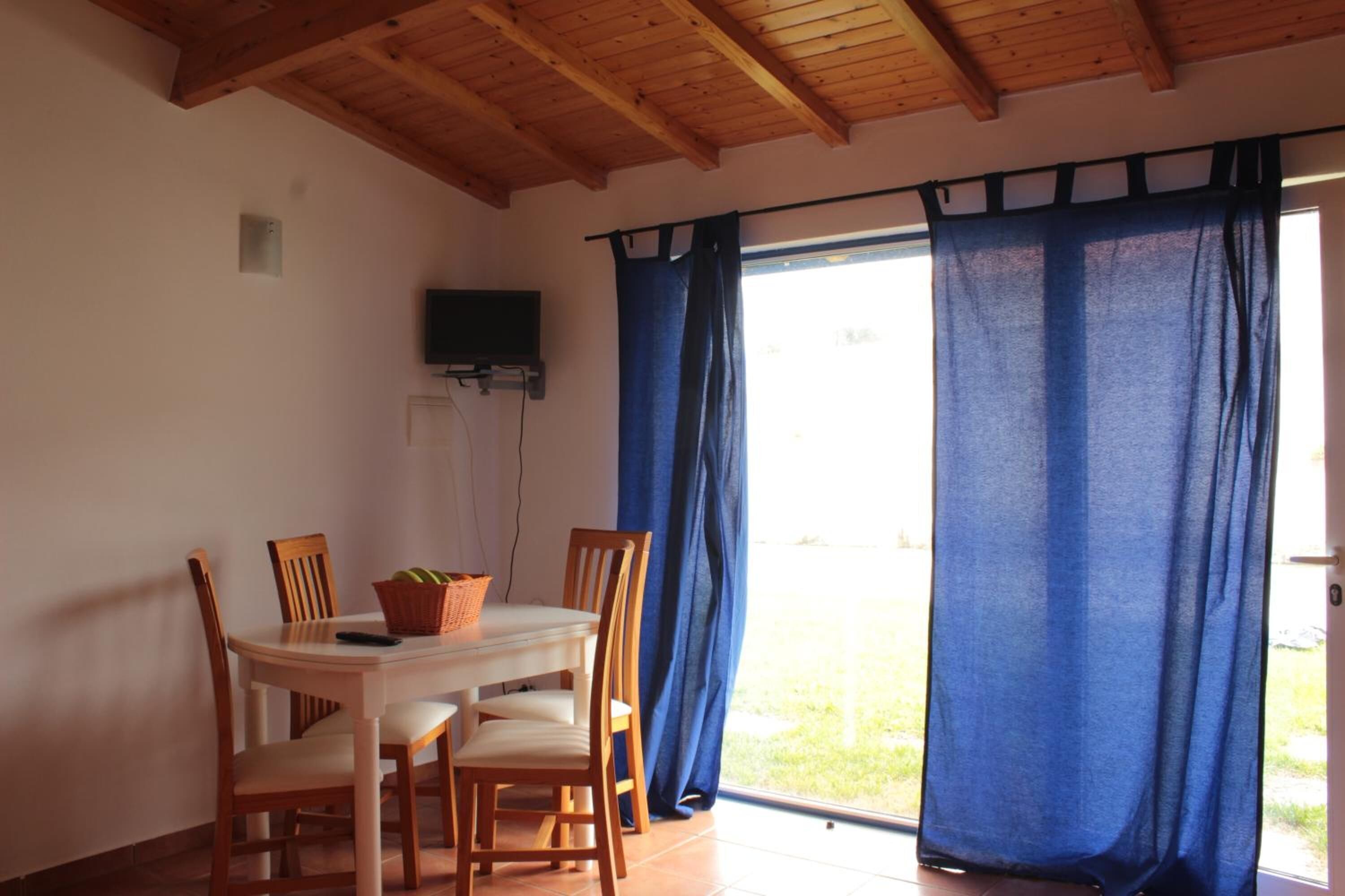 A dining area with a table and chairs, a television mounted on the wall, and blue curtains.