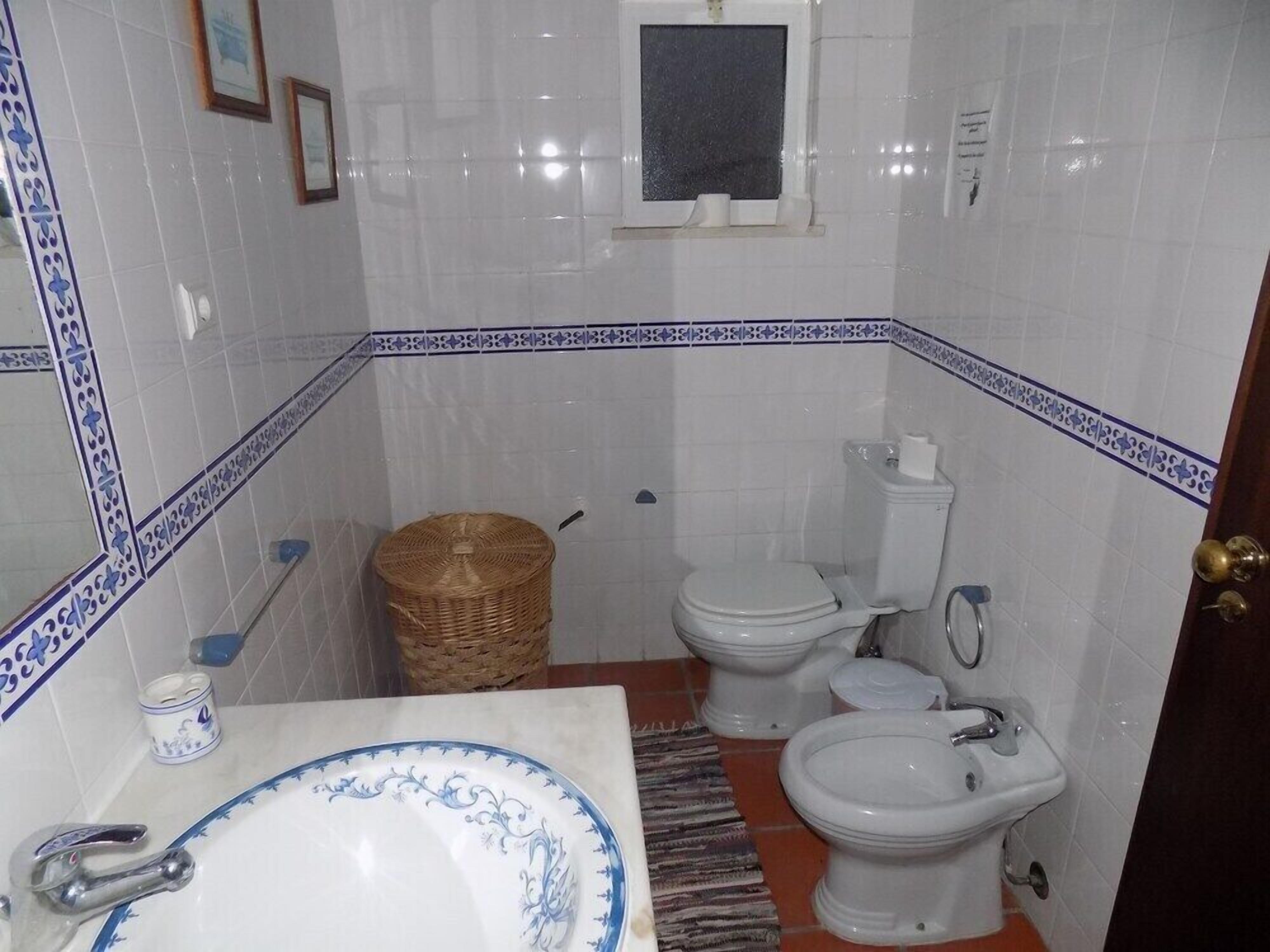 A bathroom with a white sink, two toilets, a bidet, and a small wicker basket.