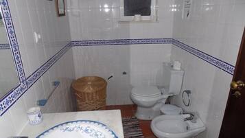 A bathroom with a white sink, two toilets, a bidet, and a small wicker basket.