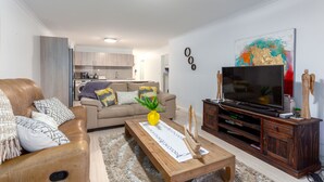 Una sala de estar moderna con un sofá de cuero, una mesa de centro de madera y un televisor de pantalla plana sobre un mueble de madera.