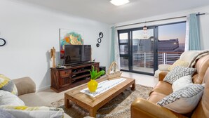Un salón con sofá, mesa de centro, televisor y vistas al exterior a través de un ventanal.