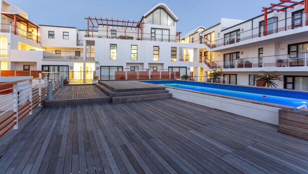 Un hotel moderno con terraza de madera, piscina y varios balcones.