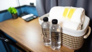 A hotel room with a wooden desk, two water bottles, a white towel, and a checkered basket. - Malades House (Bangkok)