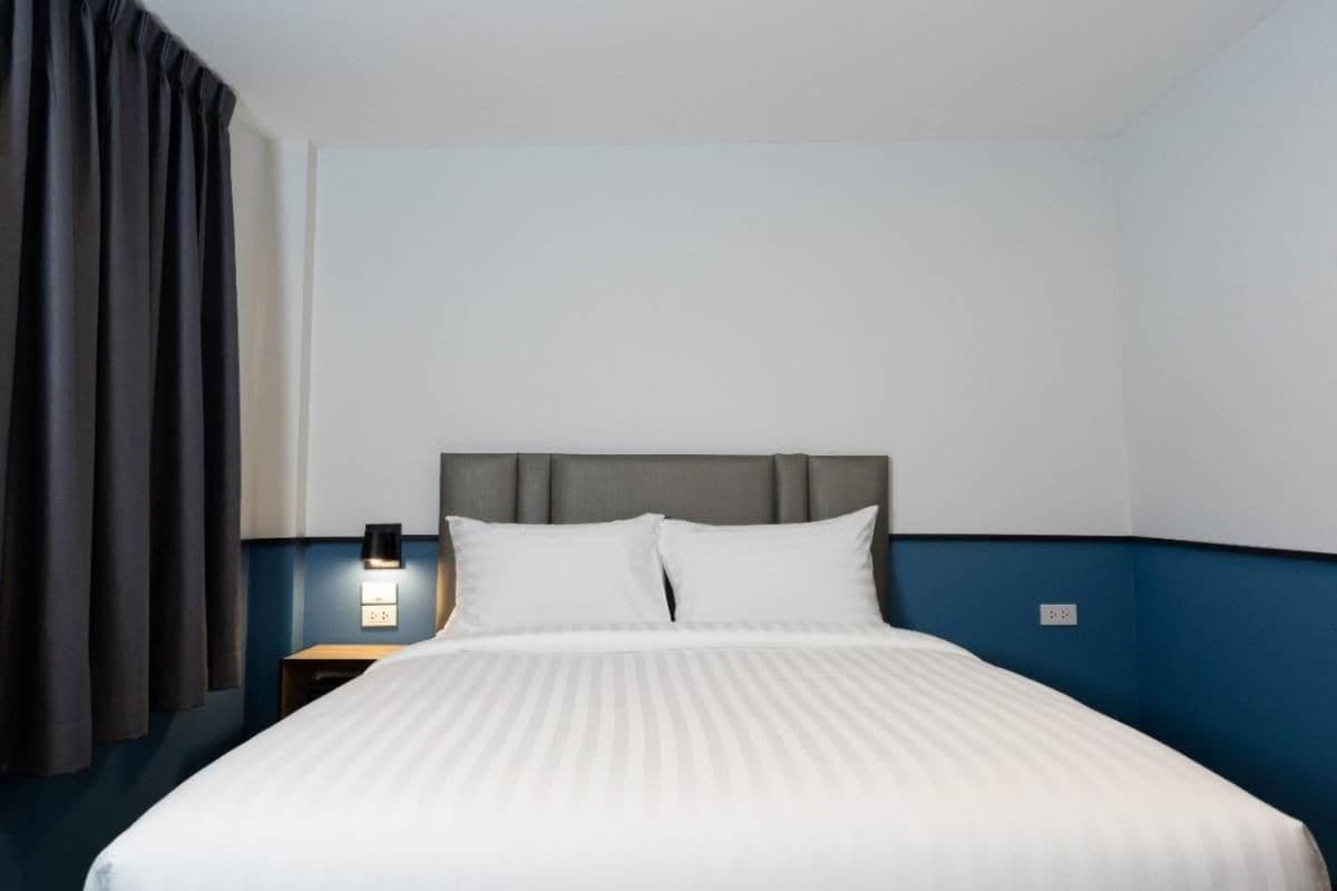 A hotel room with a bed, a nightstand, a lamp, and a window with curtains.