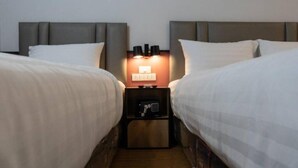 A hotel room with two beds, a nightstand with a lamp, and a small wooden cabinet. - Malades House (Bangkok)