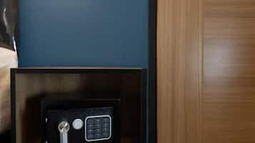 A room with a wooden door, a bedside table with a lamp, and a safe on the floor.