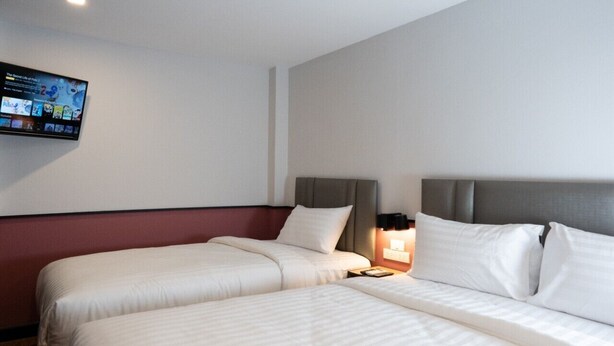 A hotel room with two beds, a flat-screen TV mounted on the wall, and a bedside table with a lamp. - Malades House (Bangkok)