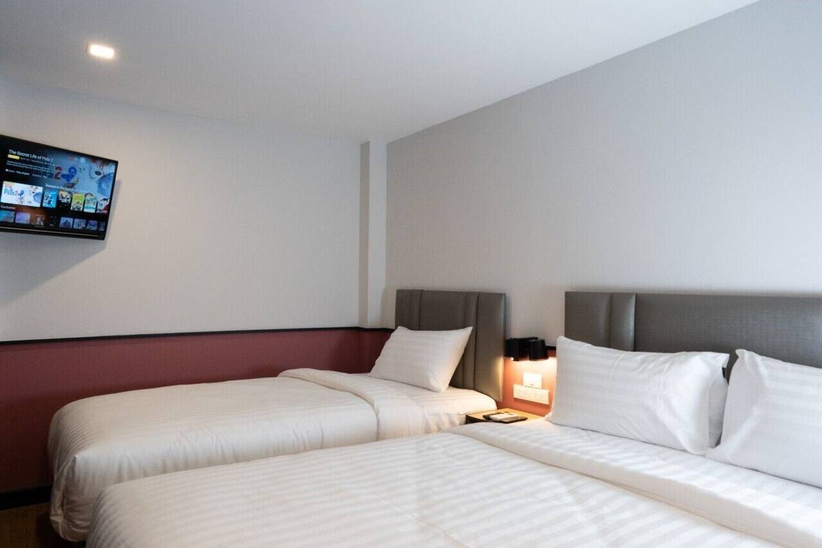 A hotel room with two beds, a flat-screen TV mounted on the wall, and a bedside table with a lamp.