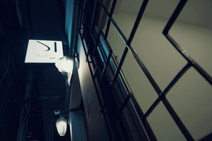 A corridor with a sign hanging from the ceiling, a metal railing, and a door at the end. - Malades House (Bangkok)
