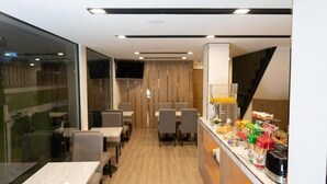 A modern dining area with tables and chairs, a counter with food items, and a view of the outside. - Malades House (Bangkok)