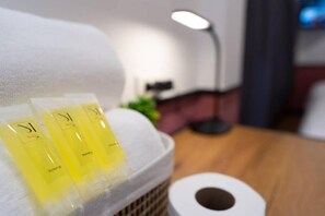 A bathroom with a towel, a roll of toilet paper, and three yellow bottles on a shelf. - Malades House (Bangkok)