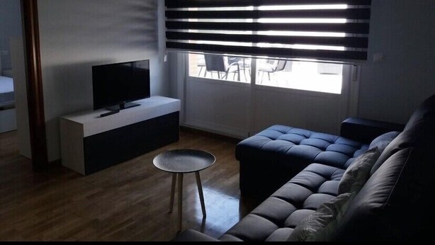 A modern living room with a flat-screen TV on a white console, a dark sofa, and a small round table.